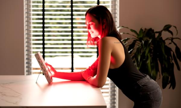 Vrouw staat voor een rood licht therapie lamp te genieten van een sessie.